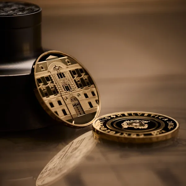 Swissmint press photograph of the 2026 50 franc gold coin "120 years of the Swissmint building", one piece standing on edge showing the façade, one lying face down showing the reverse