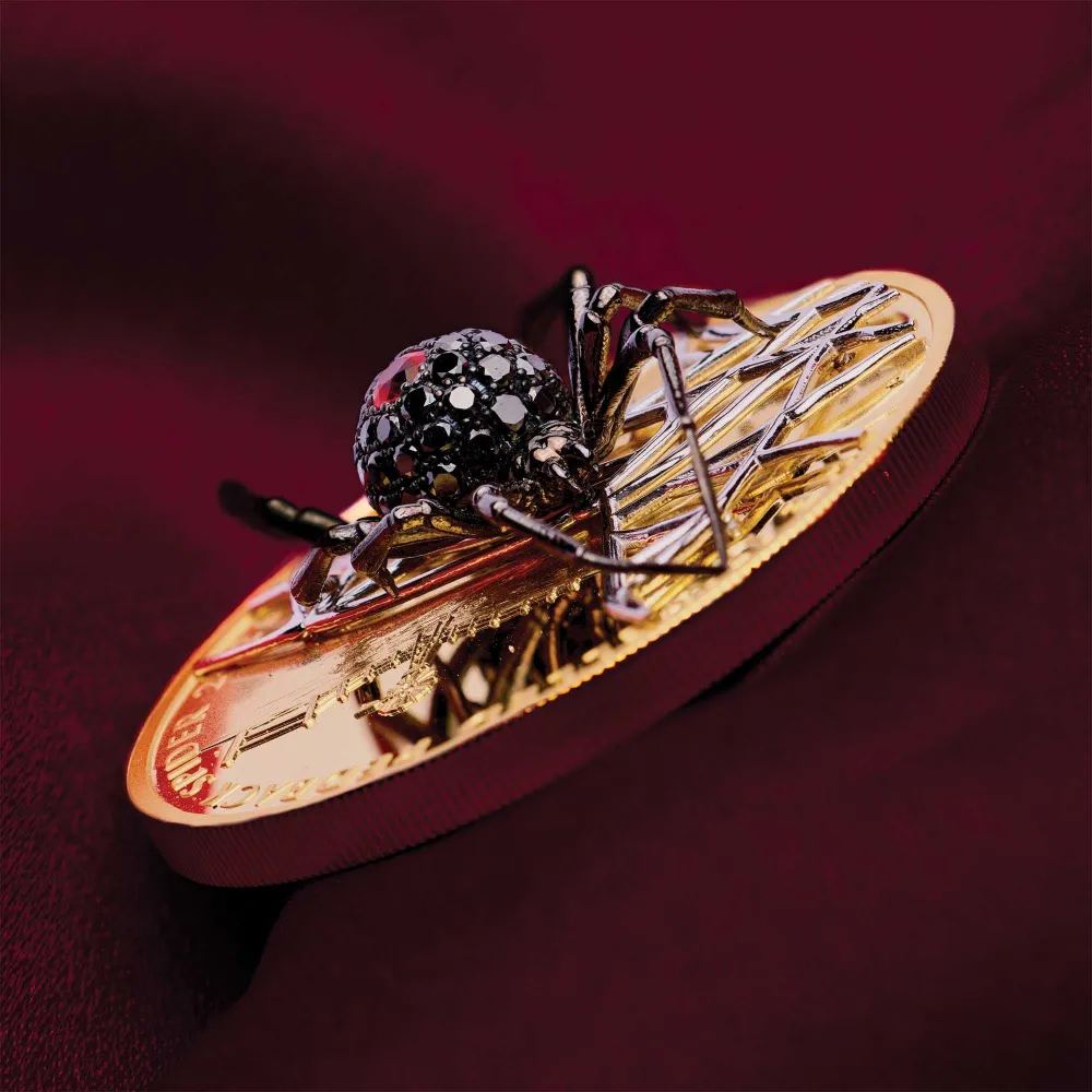 Jewelled Redback Spider 2026 coin on edge, showing the three dimensional spider standing above the gold field with the outback windmill behind